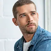 A portrait of a man with short brown hair and a light beard looking toward a window, featuring alert eyes with firm, well-defined upper and lower eyelid contours. - Male eyelid in San Francisco, CA