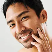 A close-up, angled shot of a man smiling and touching his face, highlighting a straight, proportionate nasal bridge and a well-defined tip that complements his facial features. - Male rhino in San Francisco, CA