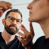 A male professional with a beard and glasses examines a patient's facial profile, focusing on the refined and straight structure of the nasal bridge. - Revision rhinoplasty in San Francisco, CA